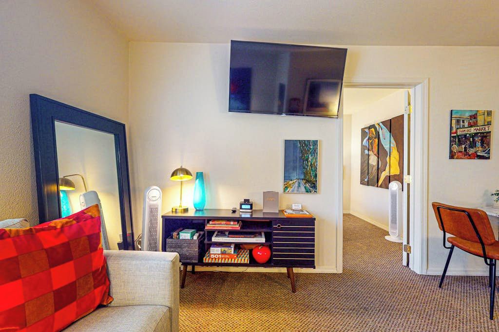 Een woonkamer met een bank, een salontafel, een flatscreen televisie aan de muur, een console tafel met decoratieve voorwerpen, en een deur die naar een andere kamer leidt.