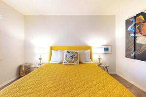 Une chambre d’hôtel avec un grand lit, deux tables de chevet, une lampe, un coussin décoratif et un tableau au mur.