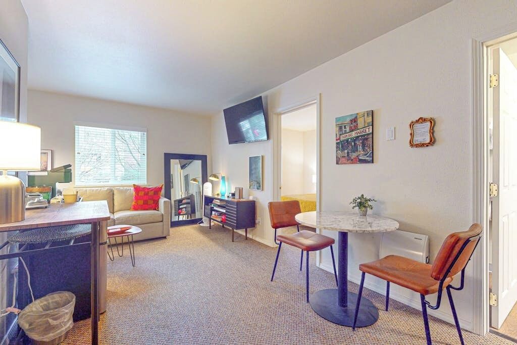 Een moderne woonkamer met een bank, een eettafel met stoelen, een televisie en kunstwerken aan de wanden.