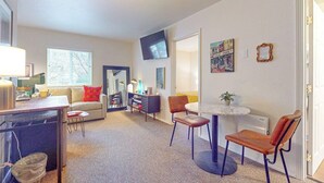 A modern living room with a sofa, a dining table with chairs, a television, and artwork on the walls. - 1BR Hotel Room right in Downtown Port Townsend (Port Townsend)