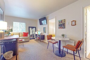 A modern living room with a sofa, a dining table with chairs, a television, and artwork on the walls. - 1BR Hotel Room right in Downtown Port Townsend (Port Townsend)