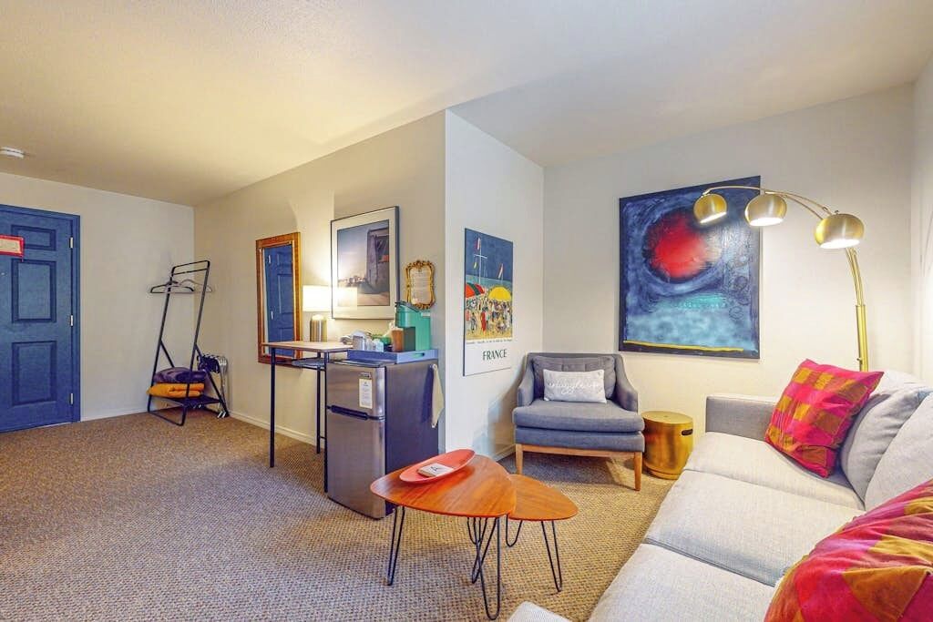 A compact living space with a kitchenette, a sofa, a chair, and a painting on the wall.