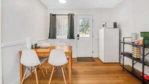 A compact kitchen with a dining table and chairs, a refrigerator, and a window with curtains.