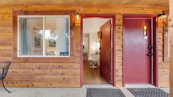 Una cabaña de madera con puerta roja, una ventana con cortina y el número '3' en la pared.