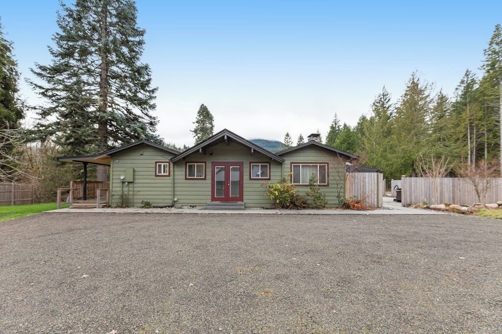 A two-story house with a front porch, a red door, and a gravel driveway.