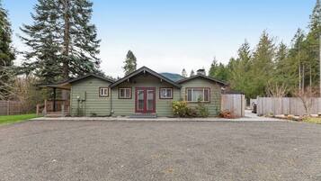 A two-story house with a front porch, a red door, and a gravel driveway.
