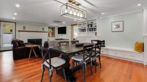 Un salon moderne comprenant un coin repas, un plancher en bois, une cheminée, une bibliothèque et un téléviseur fixé au mur.