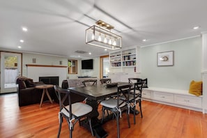 Un salon moderne comprenant un coin repas, un plancher en bois, une cheminée, une bibliothèque et un téléviseur fixé au mur.