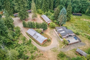 Une vue aérienne d’une propriété comprenant plusieurs bâtiments, entourée d’une forêt dense.