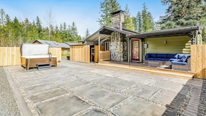 A wooden cabin with a stone patio, a covered outdoor seating area, and a stone chimney.