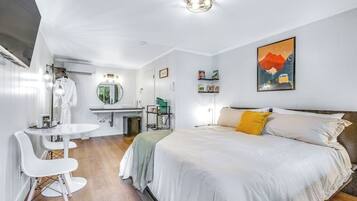 Ein modernes Hotelzimmer mit Bett, einer kleinen Küchenzeile, einem runden Spiegel und einem Essbereich mit weißem Tisch und Stühlen.