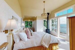 A bedroom with a large bed, two bedside lamps, a chandelier, a view of the sea, and a wooden cabinet. - 2BR  with loft soundfront retreat with mtn & city views (Bainbridge Island)