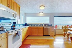 A modern kitchen with wooden cabinets, a stainless steel dishwasher, and a large window providing a view. - 3 BR beachfront cabin with private hot tub (Sequim)