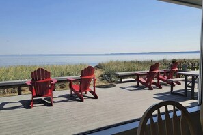 A deck with red Adirondack chairs and a table overlooking a body of water. - 3 BR beachfront cabin with private hot tub (Sequim)