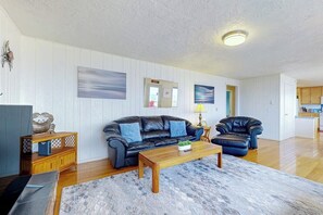 A living room with a black leather sofa, a wooden coffee table, and a blue rug. - 3 BR beachfront cabin with private hot tub (Sequim)