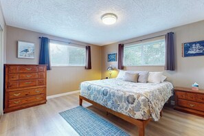 A bedroom with a bed, dresser, nightstand, and two windows with curtains. - 3 BR beachfront cabin with private hot tub (Sequim)