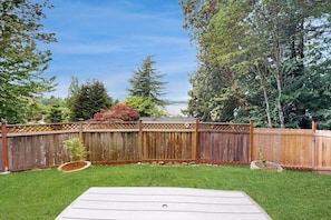A backyard with a wooden deck, a grassy lawn, and a wooden fence. - Dog-friendly house with enclosed yard (Port Orchard)