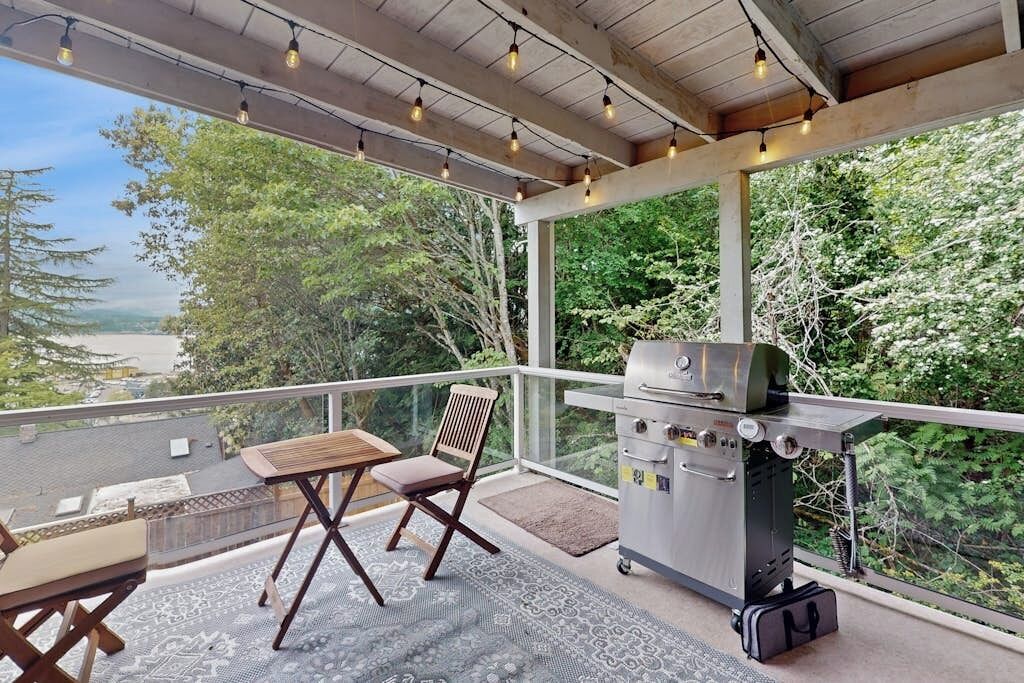 Une terrasse extérieure équipée d’un barbecue, de sièges et offrant une vue sur la forêt.