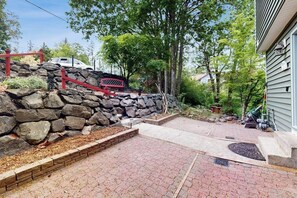 A stone retaining wall with a red metal railing, a paved patio area, and a vehicle parked in the background. - Dog-friendly house with enclosed yard (Port Orchard)