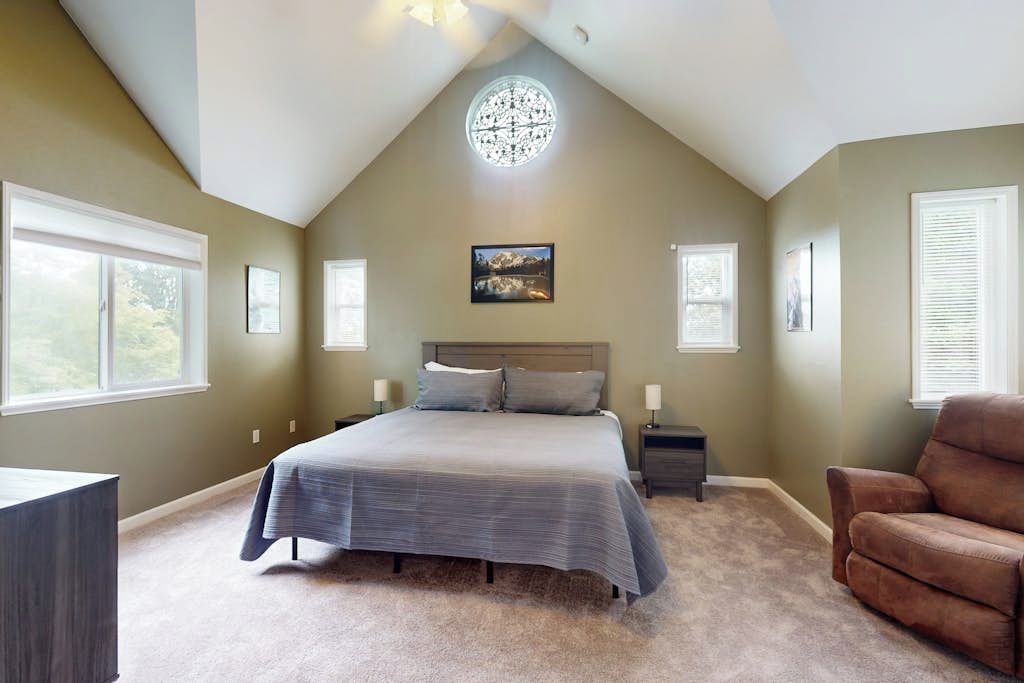 A bedroom with a large bed, a nightstand, a chair, and a ceiling light fixture.