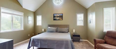 A bedroom with a large bed, a nightstand, a chair, and a ceiling light fixture.