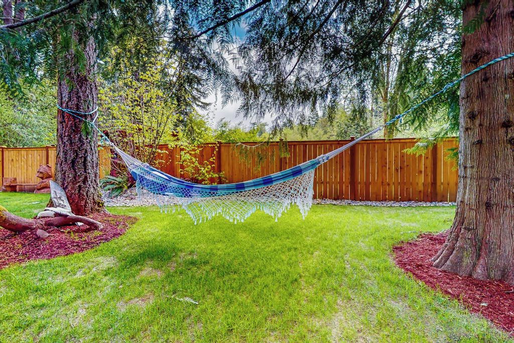 A hammock between trees in a backyard with a wooden fence and a wooden deck.