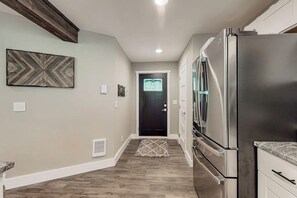A kitchen with a stainless steel refrigerator, wooden flooring, and a door with a geometric pattern. - 2BR home with hot tub, firepit, Washer Dryer, riverfront (Tahuya)
