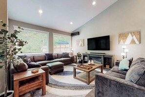 A modern living room with a leather sofa, a coffee table, and a flat-screen TV mounted on the wall. - 2BR home with hot tub, firepit, Washer Dryer, riverfront (Tahuya)