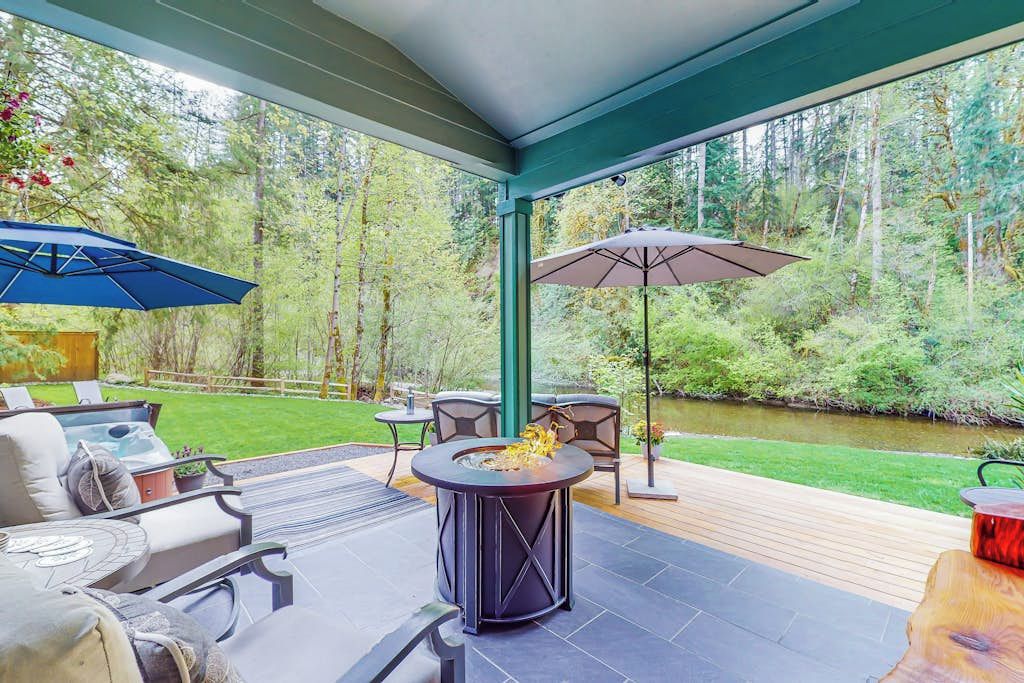 Une terrasse extérieure dotée d’un foyer, de sièges et de parasols, avec vue sur une rivière.
