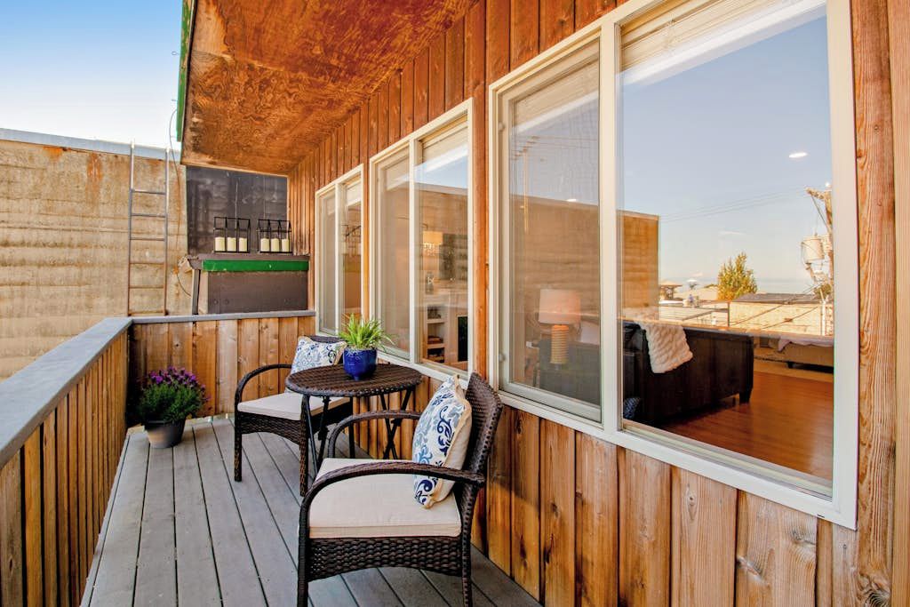 An outdoor patio with wooden walls, a seating area with chairs and a table, and a view into the adjacent room.