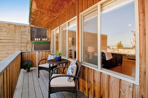 Eine Terrasse im Freien mit Holzwänden, einer Sitzecke mit Stühlen und einem Tisch sowie Blick in den angrenzenden Raum.