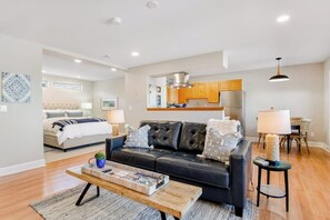A modern living room with a leather sofa, a wooden coffee table, and a dining area with wooden chairs.