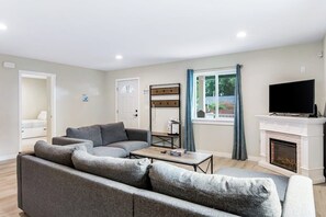 A living room with a grey sofa, a coffee table, a fireplace, a television, and a window with curtains. - Elegant 3BR Dog Friendly - Deck - Washer Dryer (Westport)