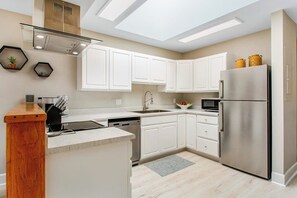 A modern kitchen with white cabinets, stainless steel appliances, and a skylight.