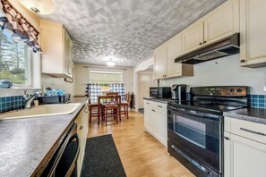 Une cuisine avec un poêle noir, des armoires blanches et une fenêtre donnant sur les arbres.