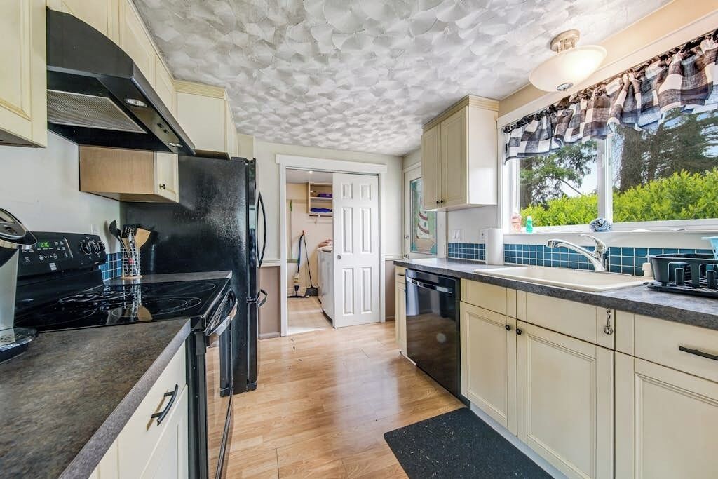 A kitchen with a black stove, white cabinets, a window with curtains, and a door leading to another room.