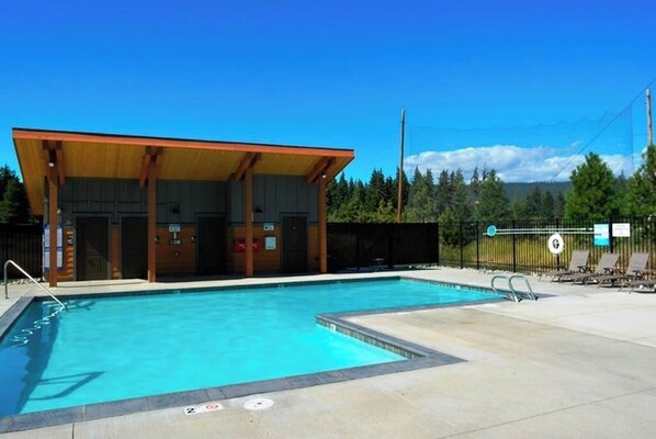 A swimming pool with a covered pavilion, a fenced area with lounge chairs, and a clear sky.