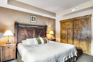 A neatly made bed with a headboard, two bedside lamps, and a wooden wardrobe.