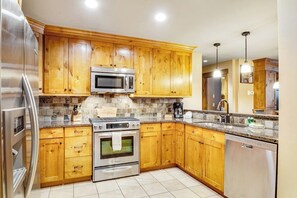 A kitchen with wooden cabinets, a stainless steel refrigerator, a microwave, an oven, a dishwasher, and a granite countertop.