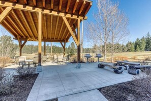 A covered outdoor seating area with tables and chairs, a fire pit, and a wooden pergola structure.