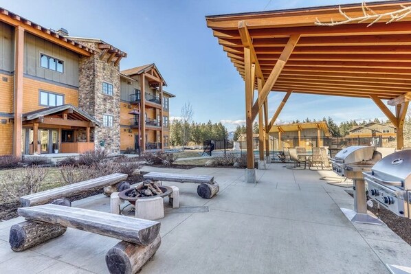 A covered outdoor area with a fire pit, wooden benches, and barbecue grills.