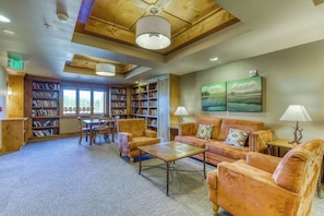 A library with bookshelves, a reading area with sofas and a coffee table, and a painting on the wall.