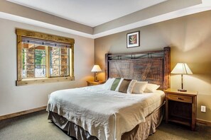 Une chambre à coucher avec un grand lit, deux tables de chevet, une fenêtre avec un encadrement en pierre et une tête de lit à motifs écossais.
