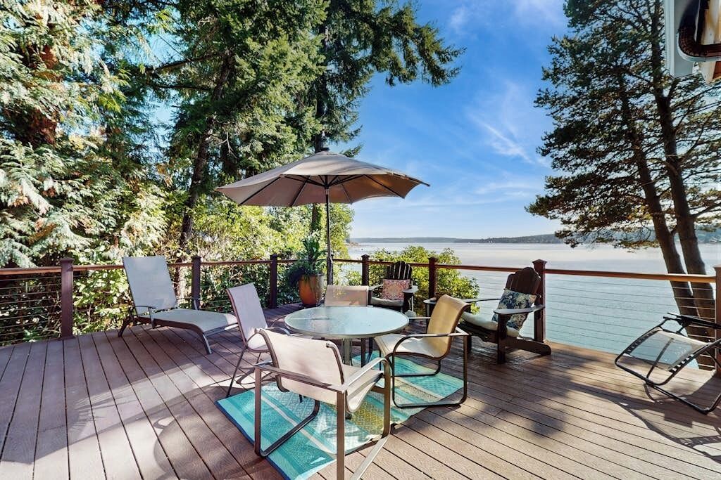 A deck with outdoor furniture, a table, and an umbrella, overlooking a body of water.