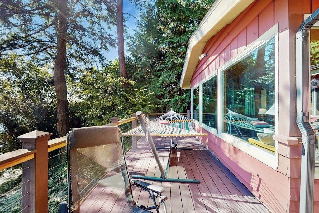 A wooden deck with a hammock and exercise equipment, overlooking a forested area.