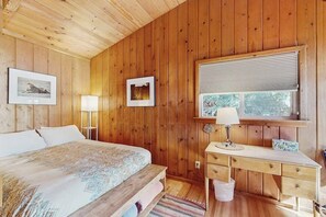 A wooden-paneled bedroom with a bed, bedside lamps, a desk, and a window with blinds. - 1BR Soundview House - Fireplace (Gig Harbor)