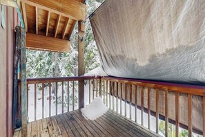 A wooden deck with a snow-covered railing and a tarp hanging over the edge. - Delightful 2BR - WoodStove - Balcony - Game Room (Snoqualmie Pass)