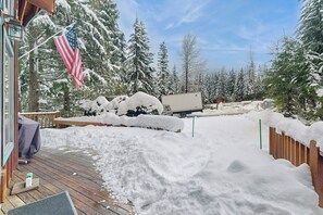 A snowy deck area with a covered seating area, a flag, and a truck parked in the background. - Delightful 2BR - WoodStove - Balcony - Game Room (Snoqualmie Pass)