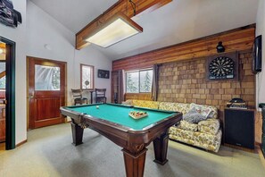 A billiards table in a room with a brick wall, a dartboard, and a sofa. - Delightful 2BR - WoodStove - Balcony - Game Room (Snoqualmie Pass)