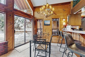 A wooden interior with a dining area, a chandelier, and a view of the outside. - Delightful 2BR - WoodStove - Balcony - Game Room (Snoqualmie Pass)